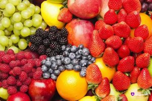 مجموعه‌ای رنگارنگ از میوه‌های تازه شامل سیب‌های قرمز، توت‌فرنگی‌ها، بلوبری‌ها، تمشک‌ها، انگورها، پرتقال‌ها، لیموها و هلوها، چیده‌شده به صورت انبوه رنگارنگ روی زمینه خنثی