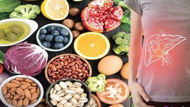 زن با طرح کبد روی شکم، کنار غذاهای سالم مثل میوه‌ها، سبزیجات، آجیل و لوبیا روی میز تیره