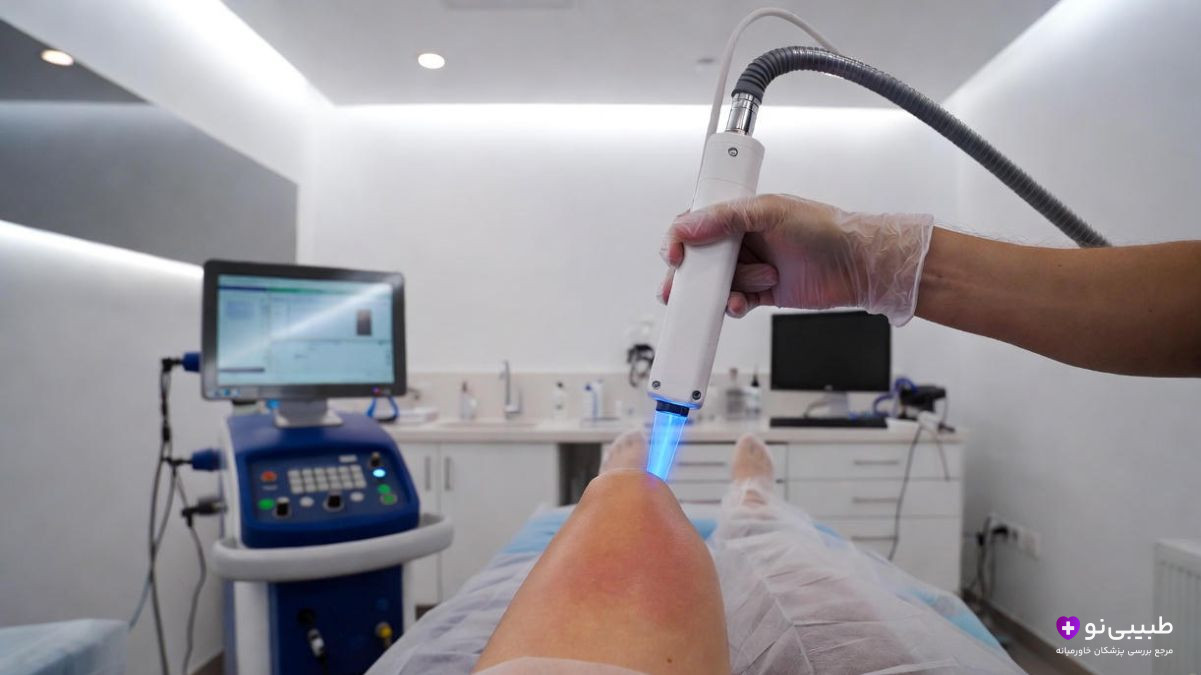 متخصص با دستکش در حال استفاده از دستگاه لیزر روی زانوی بیمار در کلینیک مجهز