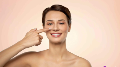 دختر جوانی با لبخند که با انگشت به نوک بینی ظریف‌شده‌اش پس از جراحی موفق بینی گوشتی اشاره می‌کند.