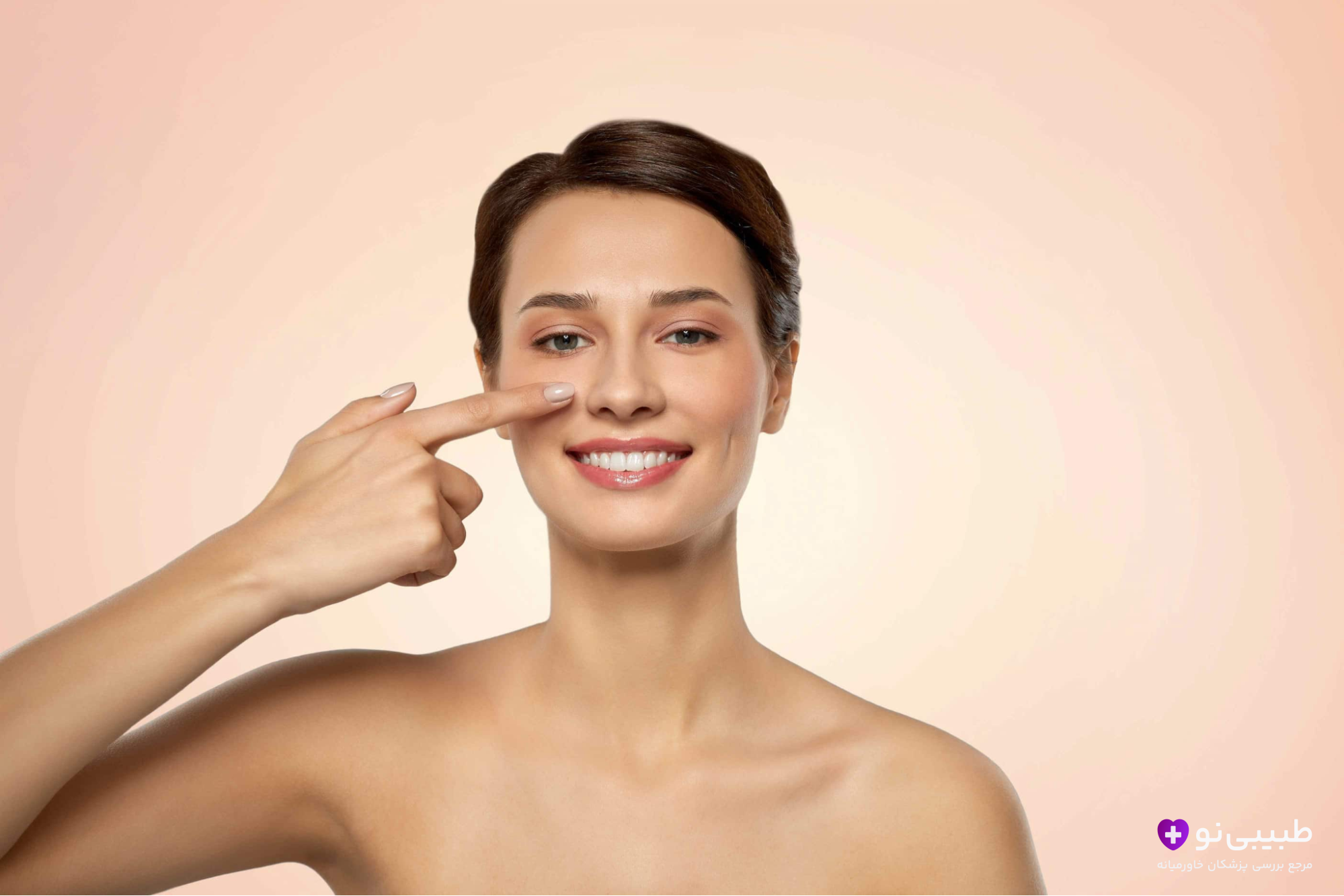 دختر جوانی با لبخند که با انگشت به نوک بینی ظریفشدهاش پس از جراحی موفق بینی گوشتی اشاره میکند.