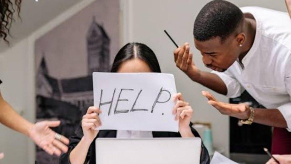 همکار آسیب دیده که تابلوی HELP را در دست گرفته و فرد سادیسمی در حال فشار و آسیب رساندن به او